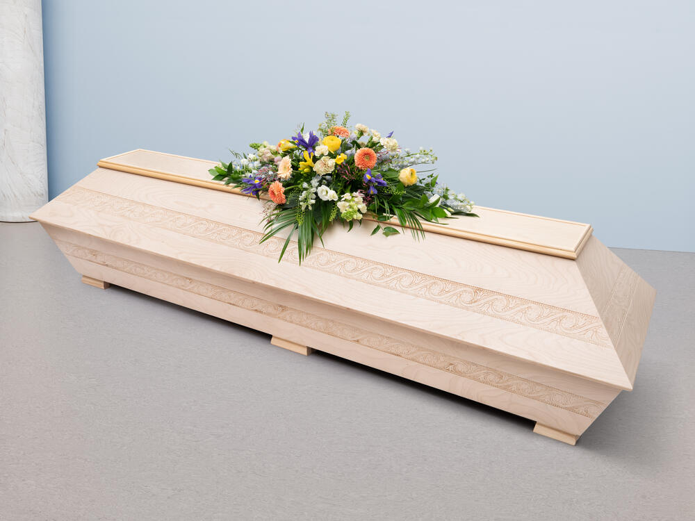 Vaalean, koristerantuisen puuarkun päällä on hyvin värikäs kukkakimppu.